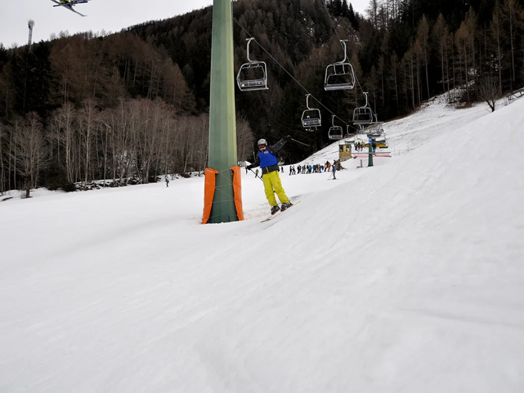 Skifahrerin in gelber Hose neben einer Liftstütze.